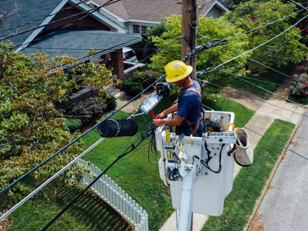 Utility worker repairing overhead power lines in a Southeast Michigan neighborhood, highlighting the region’s outdated grid and the need for a standby generator.